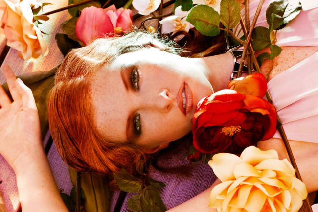 Beauty image of redhead laying in flowers at sunset